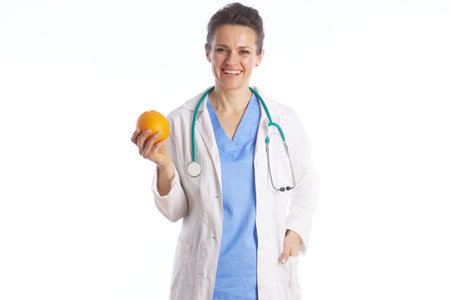 A professional female doctor in blue scrubs and a white lab coat holds a fresh orange, promoting healthy eating habits and natural vitamin intake.の写真素材