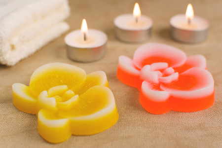 Natural organic handmade soaps in the shape of orchid. Burning candles and towel on the background.の写真素材