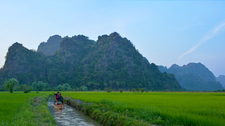 HPA-AN, MYANMAR - FEB 7, 2016 Burmese boatman driving the boat with pilgrims from Sadan Sin Min Cave in Hpa-An, Myanmar. Rice plantations and mountains on the background.のeditorial素材
