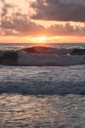 Sun setting behind the ocean with big waves on the foreground
