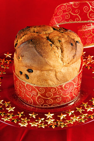 A freshly baked Panettone, the italian Christmas fruit cake with red and golden ribbon served on a red glass plate over a red background.の写真素材