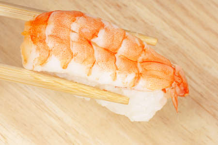 Wooden chopsticks holding a piece of sushi with shrimp, over a wooden backgroundの写真素材
