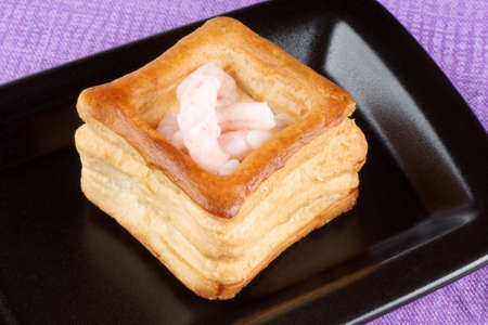 Close-up of a squared vol-au-vent stuffed with small boiled shrimps on a black plateの写真素材