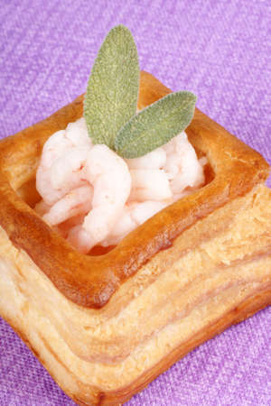 Close-up of a squared vol-au-vent stuffed with small boiled shrimps decorated with sage leaves over a purple backgroundの写真素材