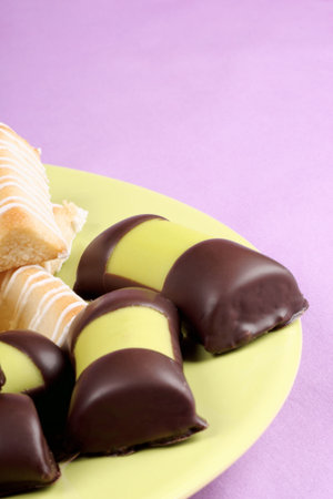 Swedish marzipan and chocolate rolls and danish macaroon fingers on a green plate over a pink...