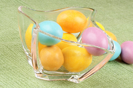 Close-up of some hard sugar coated chocolate eggs in a glass bowl, over a green background.