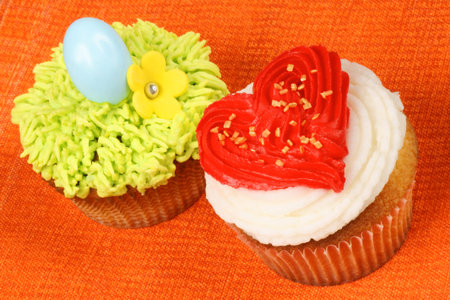 Two fancy holiday cupcakes over an orange background. A Valentine