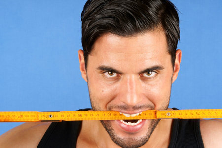 Angry handsome carpenter worker biting a wooden metric ruler over a blue background 