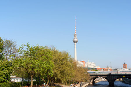 Berlin, Germany - April 16, 2009: glimpse of Central Berlin (Mitte). Some people walking along the bank of Spree River. In the background on the right the Rathaus (town hall) and in the middle the Television Tower, one of the symbols of Berlin. A train onのeditorial素材