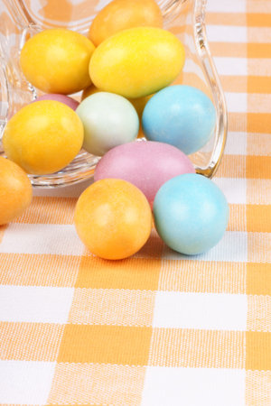 Close-up of some hard sugar coated chocolate eggs in a glass bowl, over a white and yellow chequered...
