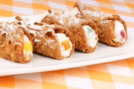 Close-up of original mini sicilian cannoli over a white plate. These tube-shaped pastries are made of fried shells filled with a sweet mixture of curd cheese, chocolate, candied fruit and sprinkled with icing sugar. Selective focus and shallow DOF.の写真素材