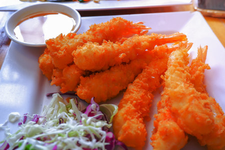 Battered shrimp tails and fried breadcrumbs are placed on a white plate, served with dipping sauce.
