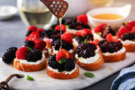 Berry and goat cheese bruschetta with fresh mint and honey, drizzling with honeyの写真素材