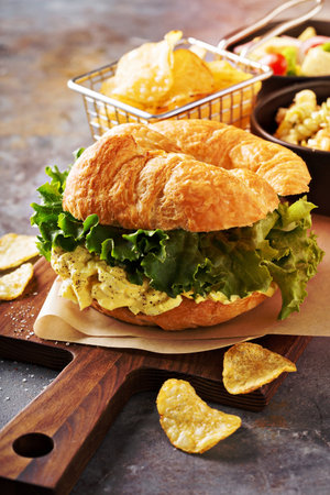 Egg salad sandwich on croissant with lettuce and chipsの写真素材