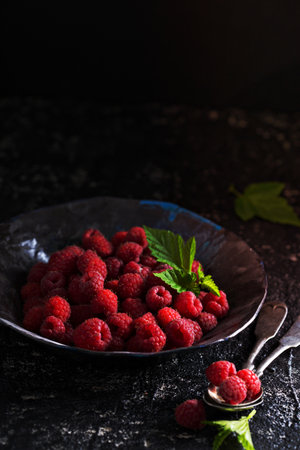 Fresh sweet raspberry in handmade black ceramic bowldark low key photoの写真素材