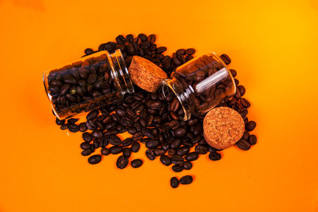 Dropped Many roasted coffee beans in a glass, in bucket jar. self-tapping screw for metal, for iron, chrome-plated self-tapping screw, isolated on orange yellow backgroundの写真素材