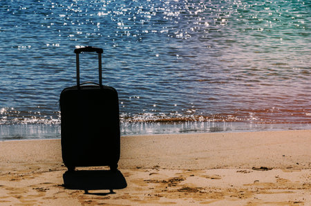 Black travel suitcase on sandy beach with turquoise sea background, summer holidays conceptの写真素材