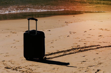 Black travel suitcase on sandy beach with turquoise sea background, summer holidays conceptの写真素材