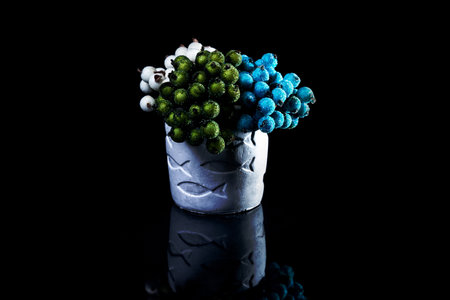A close up shot of ceramic vase with fishes with blue white and red berries in ice The porcelain vase has fluted surface. The vase with a bunch is isolated against the black background.の写真素材