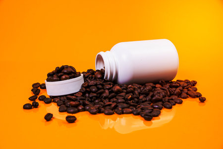 Dropped Many roasted coffee beans in a glass, in bucket jar. self-tapping screw for metal, for iron, chrome-plated self-tapping screw, isolated on orange yellow backgroundの写真素材