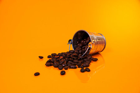 Dropped Many roasted coffee beans in a glass, in bucket jar. self-tapping screw for metal, for iron, chrome-plated self-tapping screw, isolated on orange yellow backgroundの写真素材
