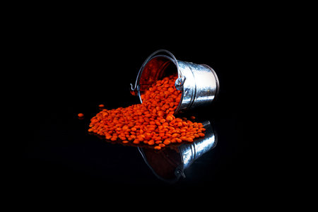 Close up of Raw Masur dal or masoor lentils or pink lentils in a black colored clay bowl on black in wineglass glass jar bucket isolated on blackの写真素材