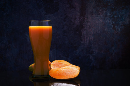 Mango juice glass and group of mangoes on black glass table. Blue background.の写真素材