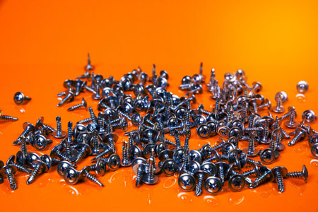 Many metal self-tapping screws made of steel in a glass, in bucket jar. self-tapping screw for metal, for iron, chrome-plated self-tapping screw, on an orange yellow background, space for textの写真素材