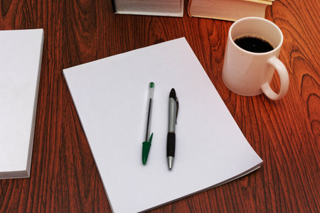 Desk with papers, books, pens and a cup of coffee on top.の写真素材