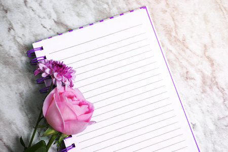 Lined notebook with flowers around it on marble table.の写真素材