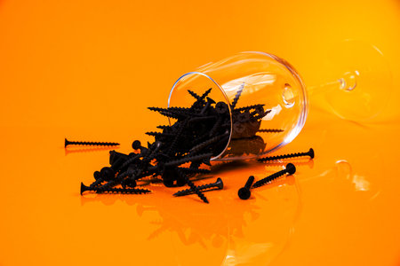 Many metal self-tapping screws made of steel in a glass, in bucket jar. self-tapping screw for metal, for iron, chrome-plated self-tapping screw, on an orange yellow background, space for textの写真素材