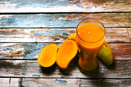 Glass of mango juice and sliced mangoes on wooden table. Colorful scene.の写真素材