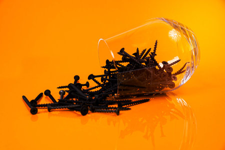 Many metal self-tapping screws made of steel in a glass, in bucket jar. self-tapping screw for metal, for iron, chrome-plated self-tapping screw, on an orange yellow background, space for textの写真素材