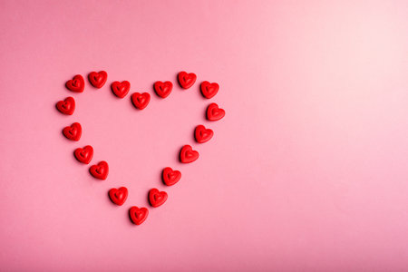Heart-shaped frame made with small hearts on a pink background.の写真素材