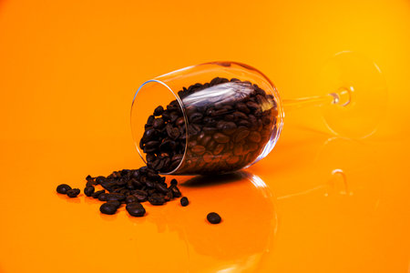 Dropped Many roasted coffee beans in a glass, in bucket jar. self-tapping screw for metal, for iron, chrome-plated self-tapping screw, isolated on orange yellow backgroundの写真素材