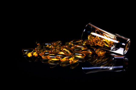 Fish oil capsules. Yellow omega 3 pills in jar on the dark black. fish oil capsules in wineglass glass . in jar. in bucket ampoules. Isolated on blackの写真素材