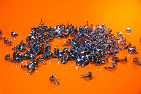 Many metal self-tapping screws made of steel in a glass, in bucket jar. self-tapping screw for metal, for iron, chrome-plated self-tapping screw, on an orange yellow background, space for textの写真素材