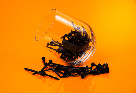 Many metal self-tapping screws made of steel in a glass, in bucket jar. self-tapping screw for metal, for iron, chrome-plated self-tapping screw, on an orange yellow background, space for textの写真素材