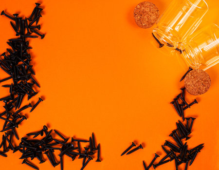 Many metal self-tapping screws made of steel in a glass, in bucket jar. self-tapping screw for metal, for iron, chrome-plated self-tapping screw, on an orange yellow background, space for textの写真素材