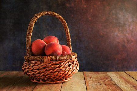 Peaches in a wicker basket on a wood table.の写真素材