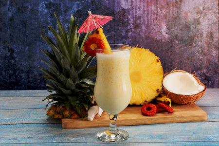Pina colada, tropical cocktail. Glass of pina colada on a blue wooden table with the components of the cocktail in the background.の写真素材
