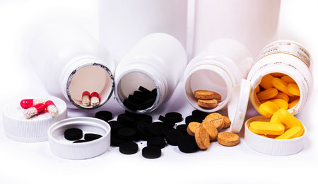 Medical white black orange pills spill out of a white jar on an isolated on white backgroundの写真素材