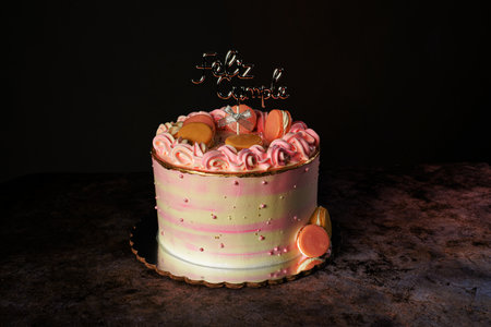 Pink birthday cake decorated with macaroons and cake topper with the text " Happy Birthday" in Spanish.の写真素材