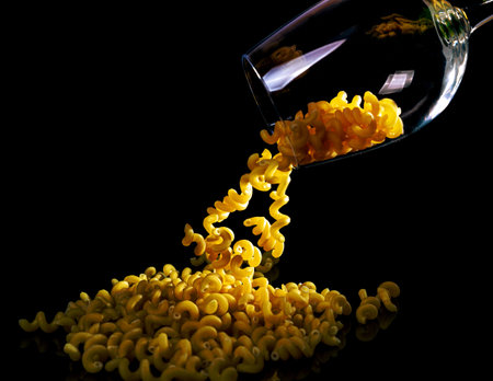 raw pasta in glass jar, wine glass. in bucket. raw pasta on black background. front view raw pasta, dropped from hand, place for text, yellow long spaghetti straws, food ingredientsの写真素材