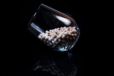 raw white beans in glass jar, wine glass. in bucket. raw white beans on black background. front view...