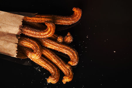 Sugared churros on black table with reflection. Churros in paper bag.の写真素材