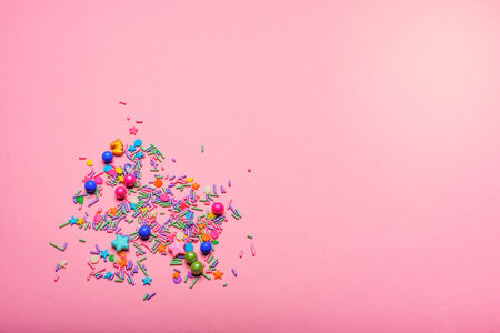 Sparkles, sprinkles, and small multicolored sugar spheres on a pink background.の写真素材