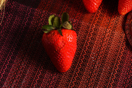 Strawberries on red textured tablecloth. Strawberries in foreground.の写真素材