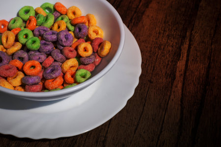 White bowl with cereal in the form of colored rings on wooden table. Cereal breakfast.の写真素材