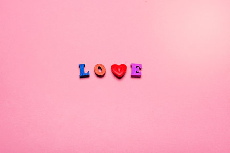 Word LOVE made of wooden letters and a heart on a pink backgroundの写真素材